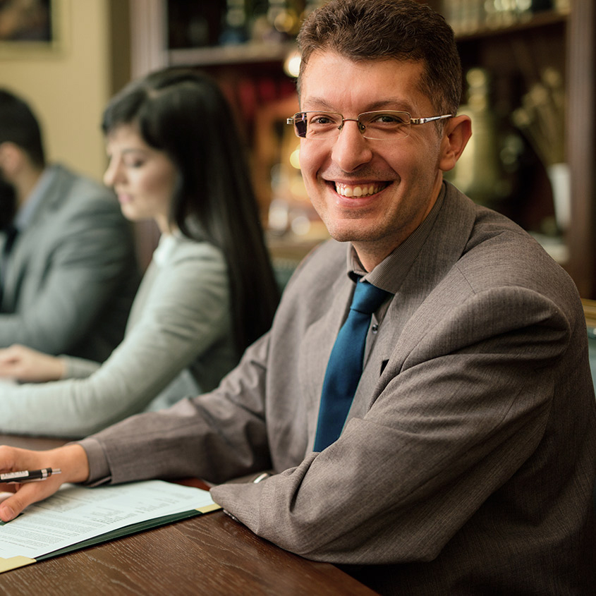 Corporate meeting with professionals in formal attire seated at a table with documents and pen."